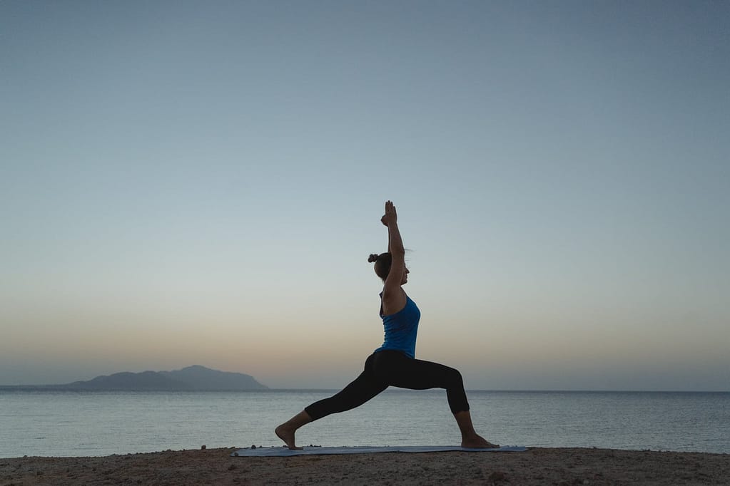 a woman doing the warrior pose at the beach